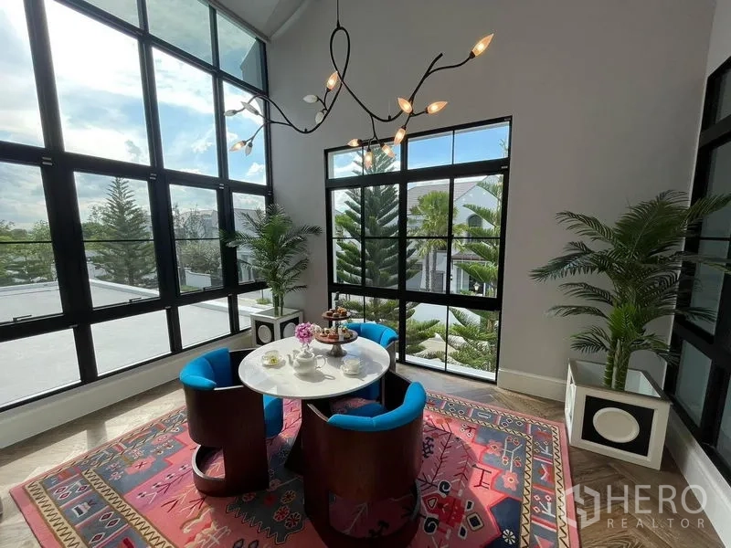 Detached House for rent or sale in Saphan Sung, Bangkok - Glass-wrapped breakfast corner with high ceiling, black-framed windows and views of mature greenery.