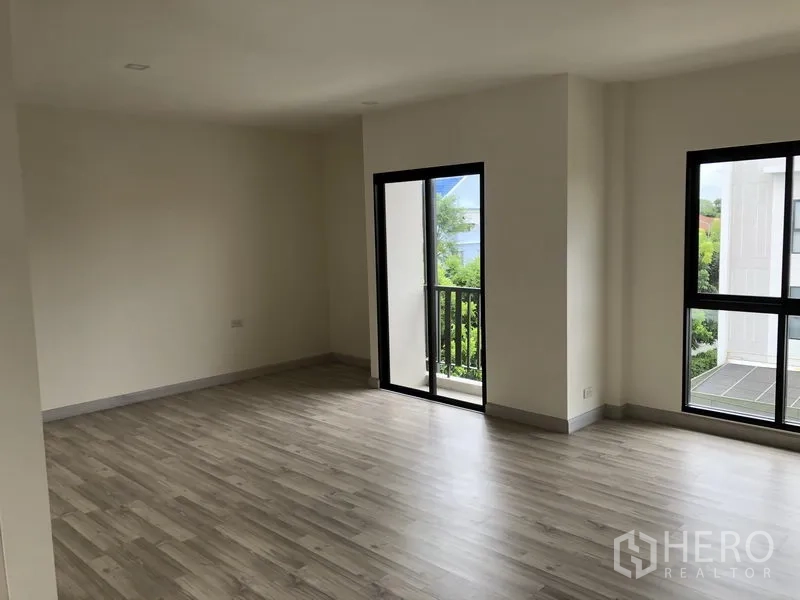 Townhouse for rent or sale in Saphan Sung, Bangkok - Corner bedroom with two large windows and a balcony, wood flooring and green views.