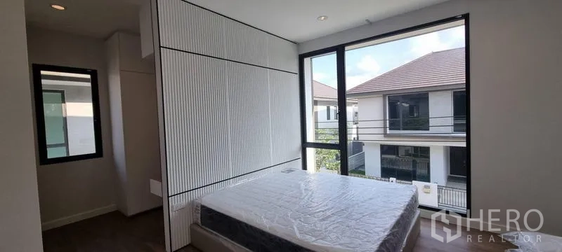 Detached House for rent in Saphan Sung, Bangkok - Bright bedroom with floor-to-ceiling corner windows and a textured headboard panel.