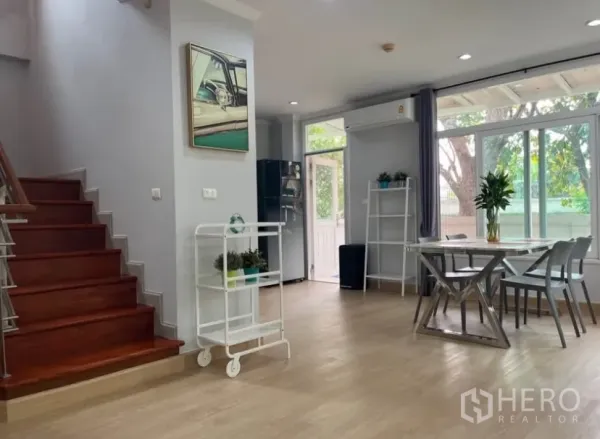 Detached House for rent or sale in Lat Phrao, Bangkok - Open-plan dining area beside wooden staircase with sliding glass door to the garden.
