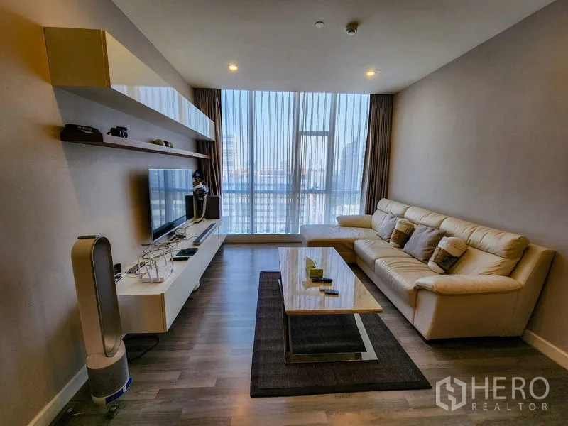 Condominium for rent or sale in Bang Rak, Bangkok - Bright living room with a cream leather sofa, TV wall, and city-view windows.