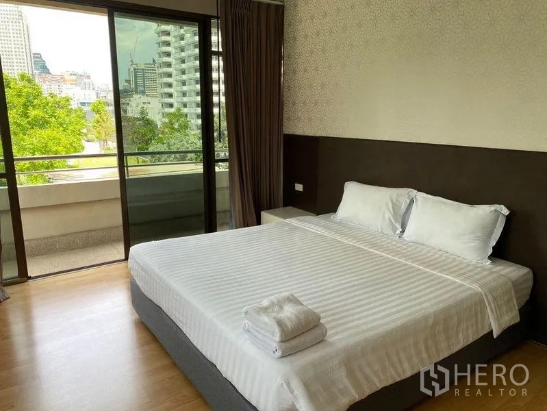 Condominium for rent in Khlong Toei, Bangkok - Bedroom with sliding doors to a balcony overlooking trees and the skyline.