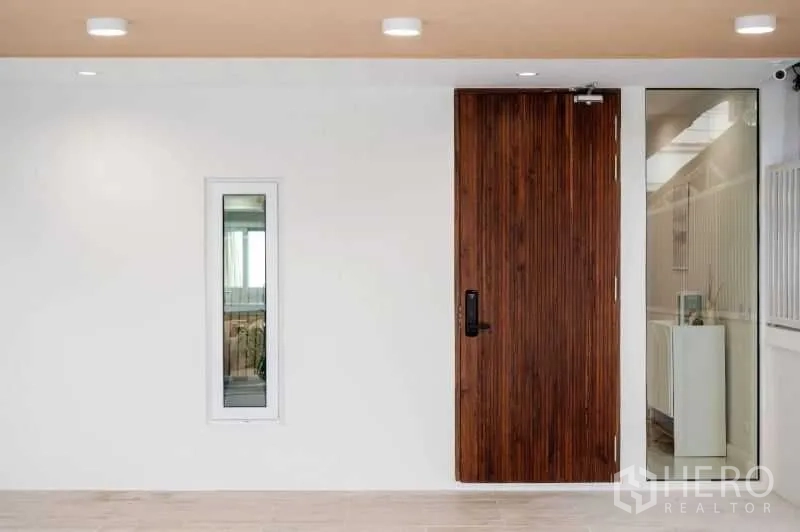 Townhouse for sale in Khlong Toei, Bangkok - Minimalist entry showing a timber front door, white walls and glass side panel with ceiling lights.