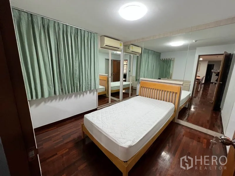 Condominium for rent or sale in Watthana, Bangkok - Bedroom with single bed, green curtains, mirrored closet doors and dual air conditioners.