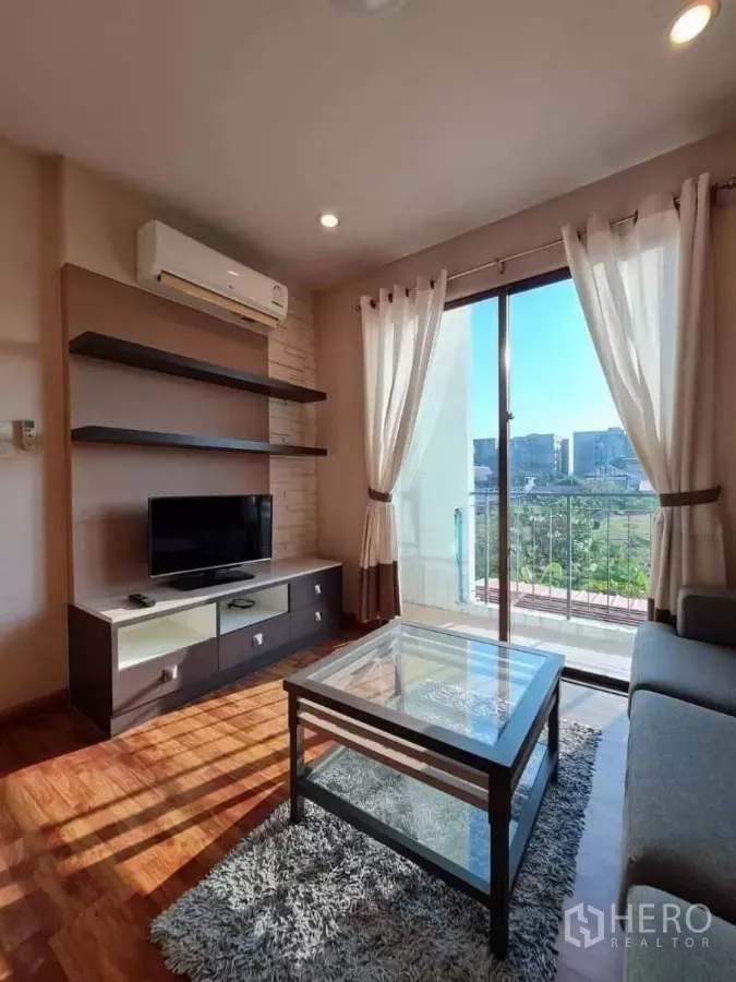 Townhouse for rent in Khlong Toei, Bangkok - Bright living room with TV console, glass coffee table, wood floors and sliding door to a balcony with city and green views.