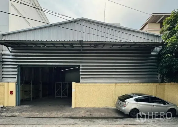 Warehouse for rent in Din Daeng, Bangkok - Street view of a metal-clad warehouse in Huai Khwang with a wide loading entrance and yellow boundary wall.