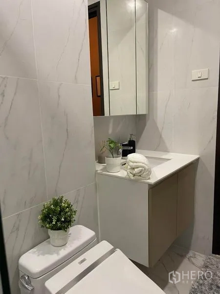 Condominium for rent in Ratchathewi, Bangkok - Bright vanity with mirror cabinets and potted plant in a marble-tiled bathroom.