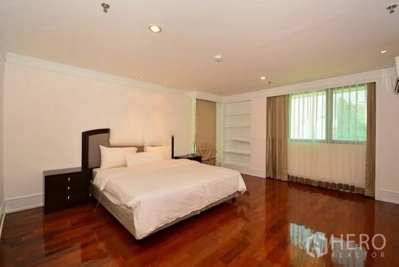 Apartment for rent in Khlong Toei, Bangkok - Large master bedroom with king bed, built-in shelving, two windows and polished wooden floors.