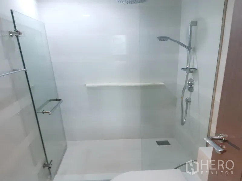 Condominium for rent in Khlong Toei, Bangkok - Clean white bathroom featuring a glass-enclosed shower with handheld and rain showerheads.