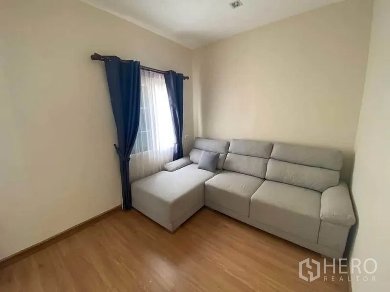 Townhouse for sale in Saphan Sung, Bangkok - Secondary bedroom set as a lounge with a gray L-shaped sofa and a curtained window.