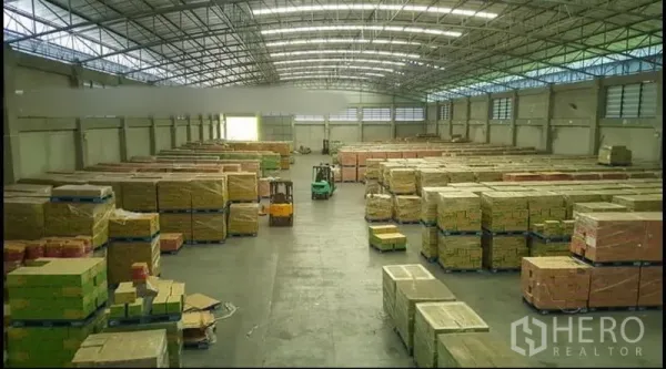 Warehouse for rent or sale - Spacious warehouse interior with high steel roof, skylights and stacks of pallets.