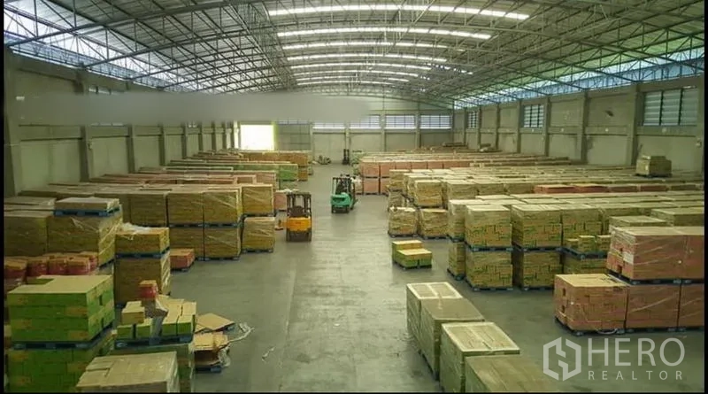 Warehouse for rent or sale - Spacious warehouse interior with high steel roof, skylights and stacks of pallets.