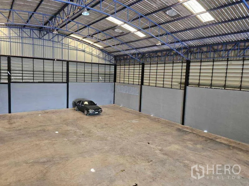 Warehouse for rent or sale in Khlong Toei, Bangkok - Elevated view of the expansive warehouse floor and high truss roof, with a car showing scale.