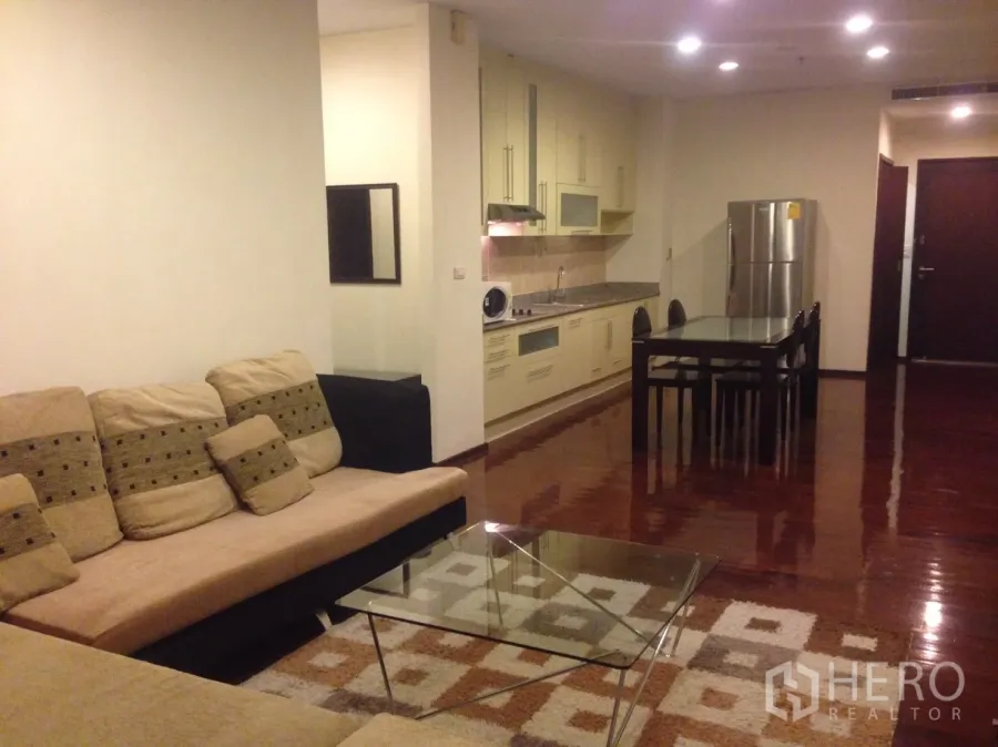 公寓 出租在Watthana, Bangkok - 通罗公寓开放式客厅，米色转角沙发、玻璃茶几、餐桌以及带冰箱的橱柜式厨房，实木地板光亮。