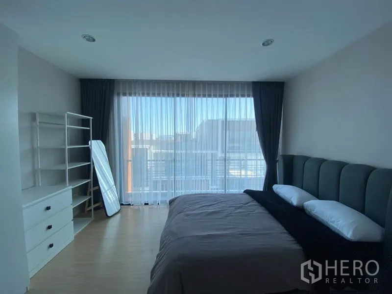 Townhouse for rent in Saphan Sung, Bangkok - Primary bedroom with balcony access, shelving unit and floor-to-ceiling curtains.