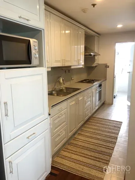 Condominium for rent or sale in Watthana, Bangkok - Galley kitchen with white cabinetry, sink, cooktop, oven and microwave.