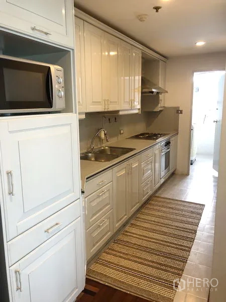 Condominium for rent or sale in Watthana, Bangkok - Galley kitchen with white cabinetry, sink, cooktop, oven and microwave.