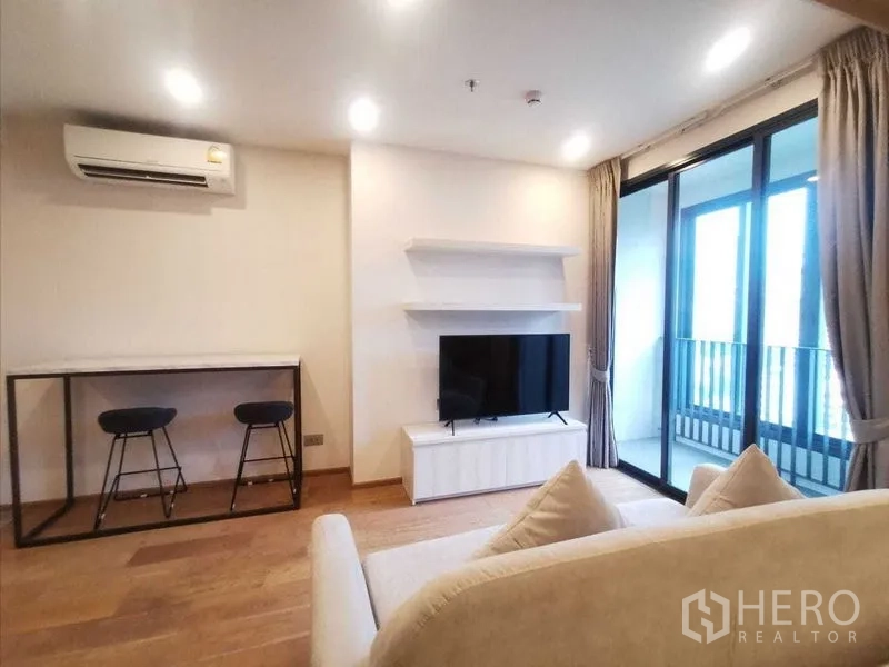 Condominium for rent in Ratchathewi, Bangkok - Bright living room with TV console, breakfast bar and sliding door to a balcony.