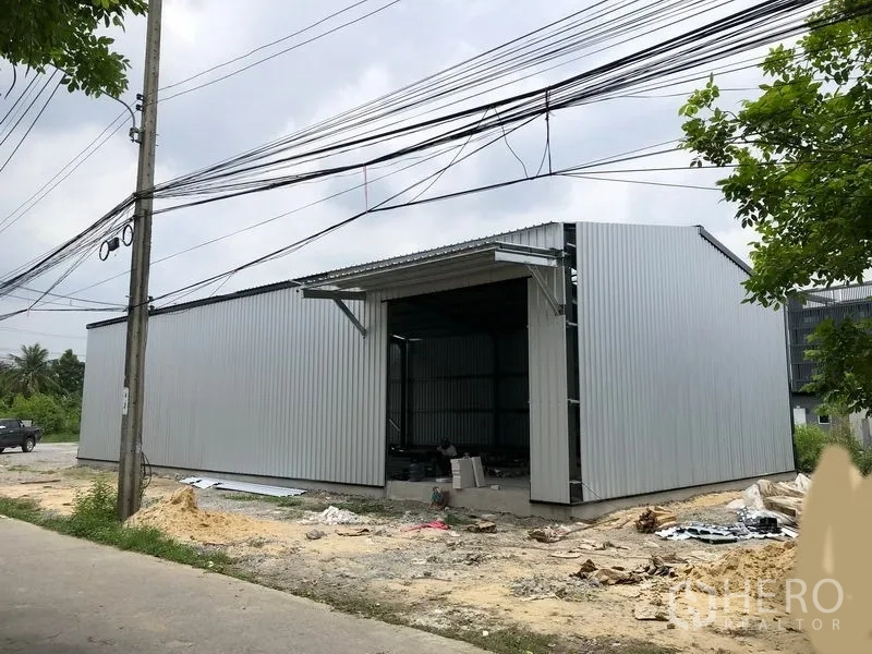 Warehouse for rent in Bang Yai, Nonthaburi - Corrugated metal warehouse exterior with wide loading door and roadside access in Bang Yai.