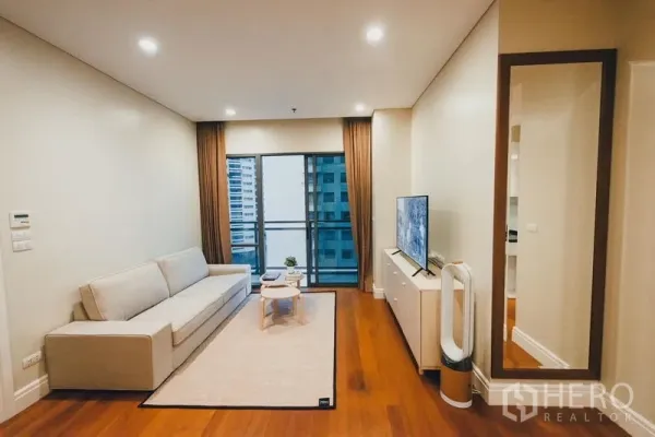 Condominium for rent in Khlong Toei, Bangkok - Bright living room with sofa, TV console, hardwood floors and sliding doors to a balcony with city view.