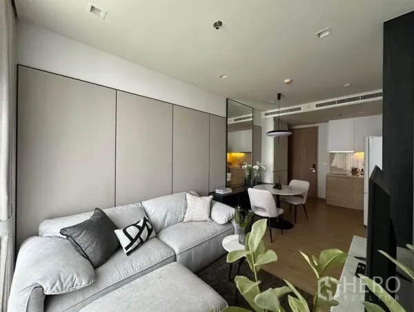 公寓 出租在Watthana, Bangkok - 开放式客餐厅连接小厨房，L形沙发、镜面墙与木地板。