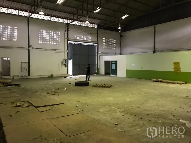 货栈 出租在Bang Phli, Samut Prakan - 空置仓库内景，超大钢制装卸门、通风砖窗、高天花与耐用混凝土地面。