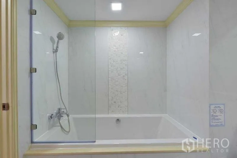 Apartment for rent in Khlong Toei, Bangkok - Close-up of tiled bathtub with hand shower and clear glass partition.