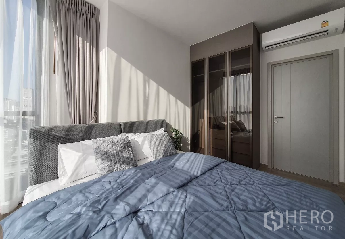 Condominium for rent in Khlong Toei, Bangkok - Master bedroom with large windows, gray headboard and mirrored wardrobe.