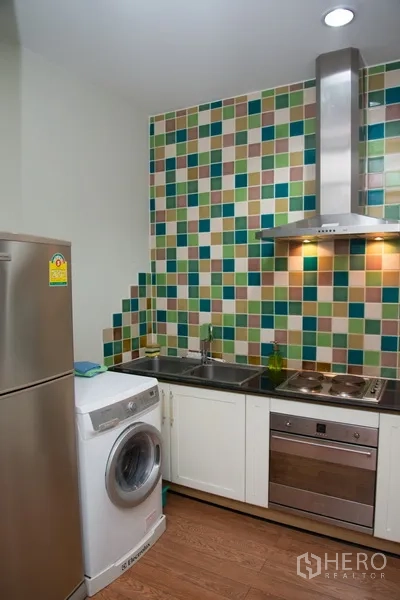 Condominium for rent in Khlong Toei, Bangkok - Compact kitchen with colorful mosaic tile backsplash, stainless hood, fridge and washing machine.