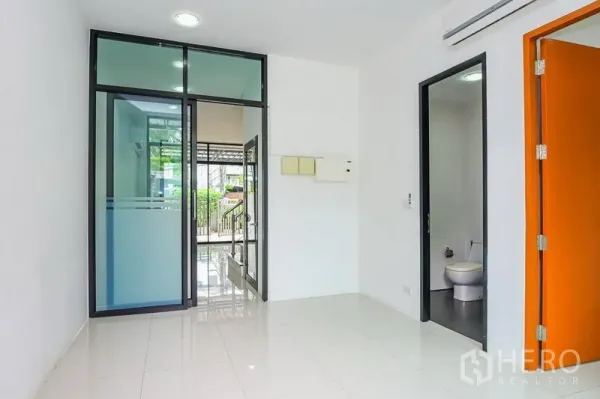 Townhouse for rent in Watthana, Bangkok - Bright ground-floor entry with glass sliding door, glossy tile flooring and a guest bathroom.