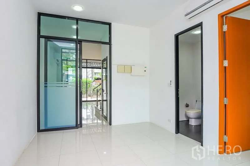 Townhouse for rent in Watthana, Bangkok - Bright ground-floor entry with glass sliding door, glossy tile flooring and a guest bathroom.