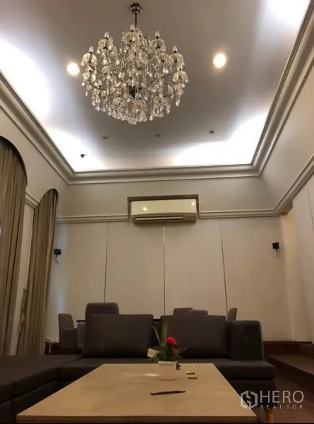 Townhouse for rent in Chatuchak, Bangkok - High-ceiling lounge with chandelier, recessed lights and a wall-mounted air conditioner.