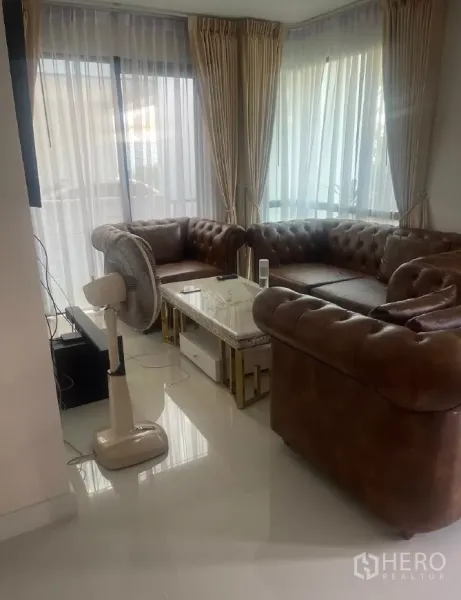 Detached House for rent or sale in Saphan Sung, Bangkok - Corner living area with large windows, sheer curtains and brown leather sofas.