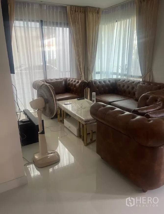 Detached House for rent or sale in Saphan Sung, Bangkok - Corner living area with large windows, sheer curtains and brown leather sofas.