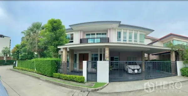 Detached House for sale in Khan Na Yao, Bangkok - Two-storey detached house with gated carport, balcony, and lush hedges on a corner plot in Khan Na Yao.