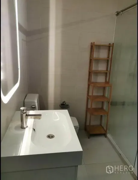 Condominium for rent in Khlong Toei, Bangkok - Modern bathroom with vanity, illuminated mirror, and shelving.