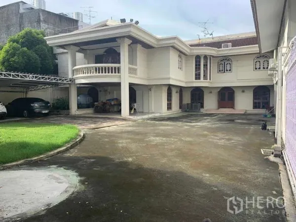 Detached House for sale in Huai Khwang, Bangkok - Grand facade with curved balcony, arched windows and a wide driveway.