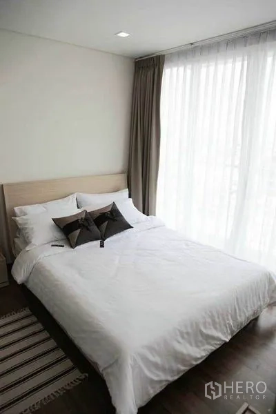 คอนโด ให้เช่าในWatthana, Bangkok - ห้องนอนอบอุ่น เตียงคู่ ชุดเครื่องนอนสีขาว พื้นไม้เข้ม และม่านโปร่งในคอนโดวัฒนา