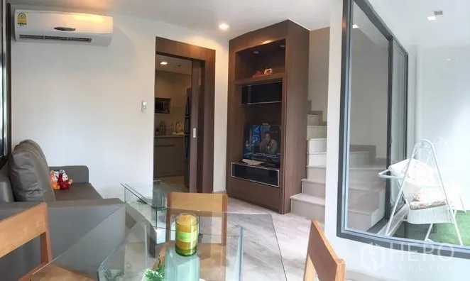 Condominium for rent in Phra Khanong, Bangkok - Cozy lounge with built-in TV wall, stairs to loft space, and sliding glass to balcony.
