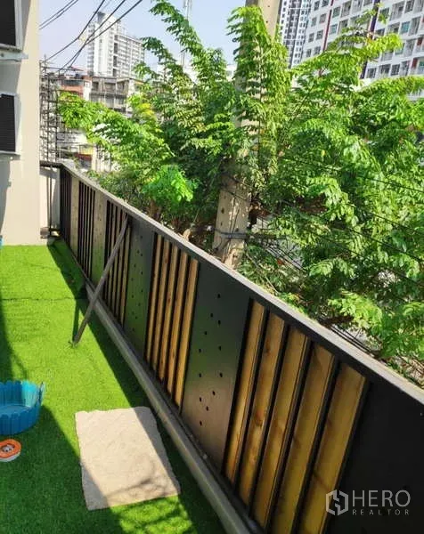 Home Office for rent in Khlong Toei, Bangkok - Balcony with artificial grass, metal railing, and leafy city views.