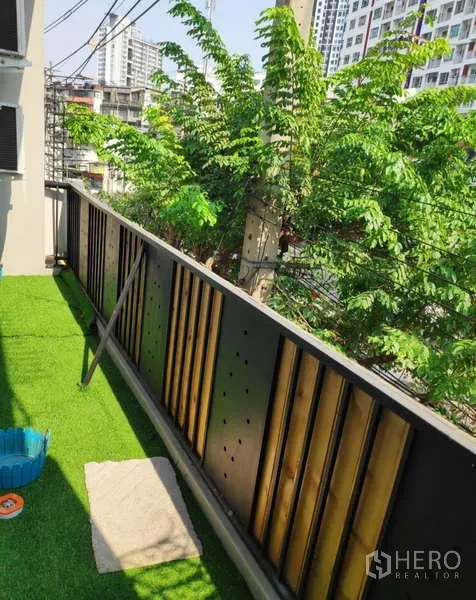 Home Office for rent in Khlong Toei, Bangkok - Balcony with artificial grass, metal railing, and leafy city views.