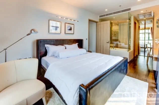 Condominium for rent or sale in Watthana, Bangkok - Bedroom featuring a glass-walled bathroom, upholstered bed and wood flooring.