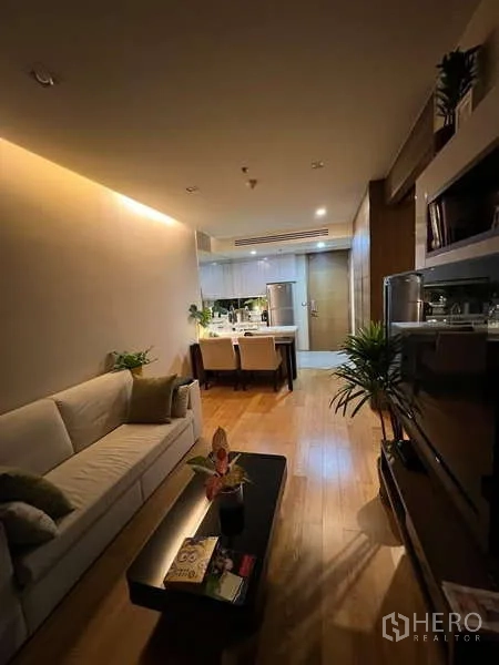 Condominium for rent in Bang Rak, Bangkok - Warm-lit lounge with sofa, TV wall unit and wood flooring.