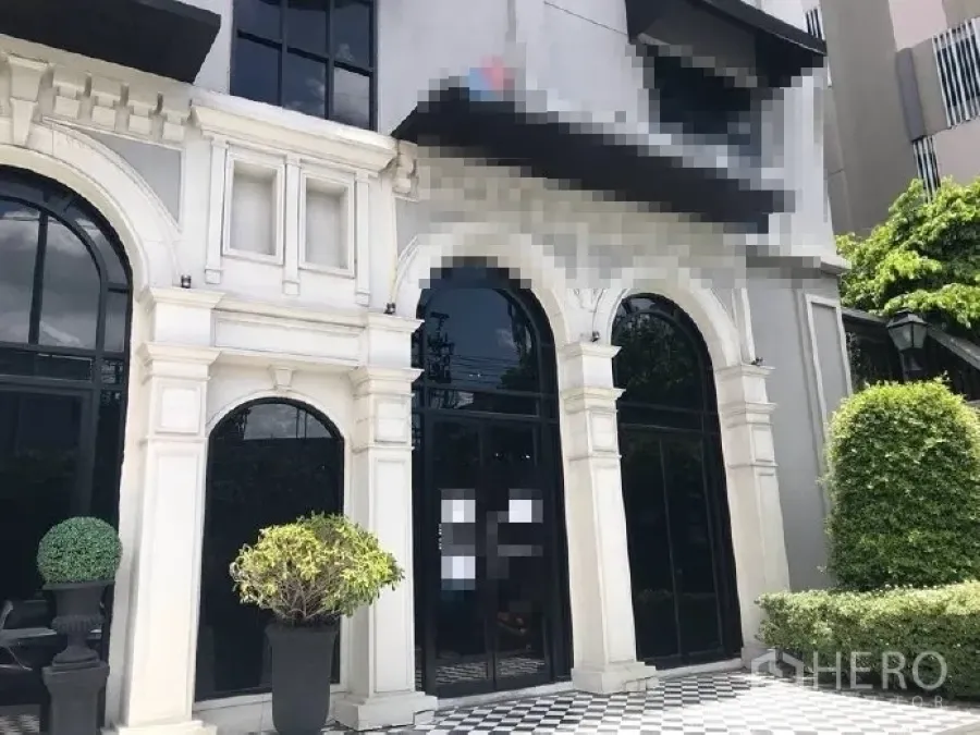 零售空间 出租在Huai Khwang, Bangkok - 零售店面特写，高挑拱形玻璃门、白色立面线条与棋盘格入口，配有绿植。