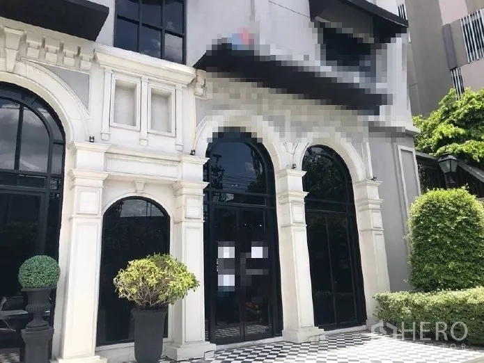零售空间 出租在Huai Khwang, Bangkok - 零售店面特写，高挑拱形玻璃门、白色立面线条与棋盘格入口，配有绿植。