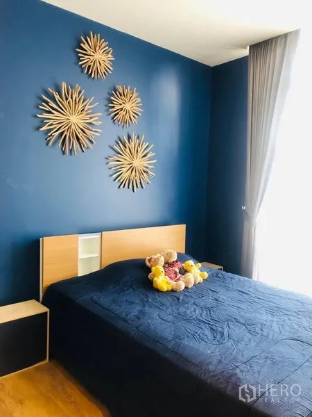 Condominium for rent in Khlong Toei, Bangkok - Bright bedroom with large window, gray curtains and navy bedding providing natural light.