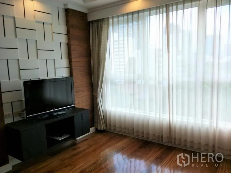 Condominium for rent or sale in Watthana, Bangkok - Sunlit room with floor‑to‑ceiling windows, sheer curtains and a TV on a media console.