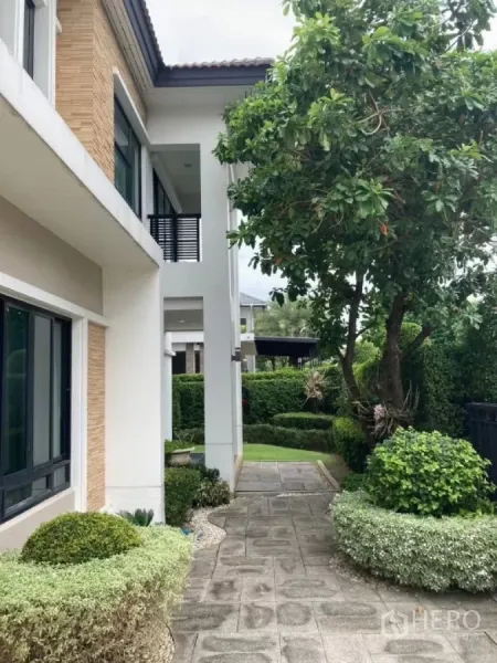 Detached House for rent in Mueang Nonthaburi, Nonthaburi - Shaded garden walkway along the side of the house with mature tree, hedges and paved path.