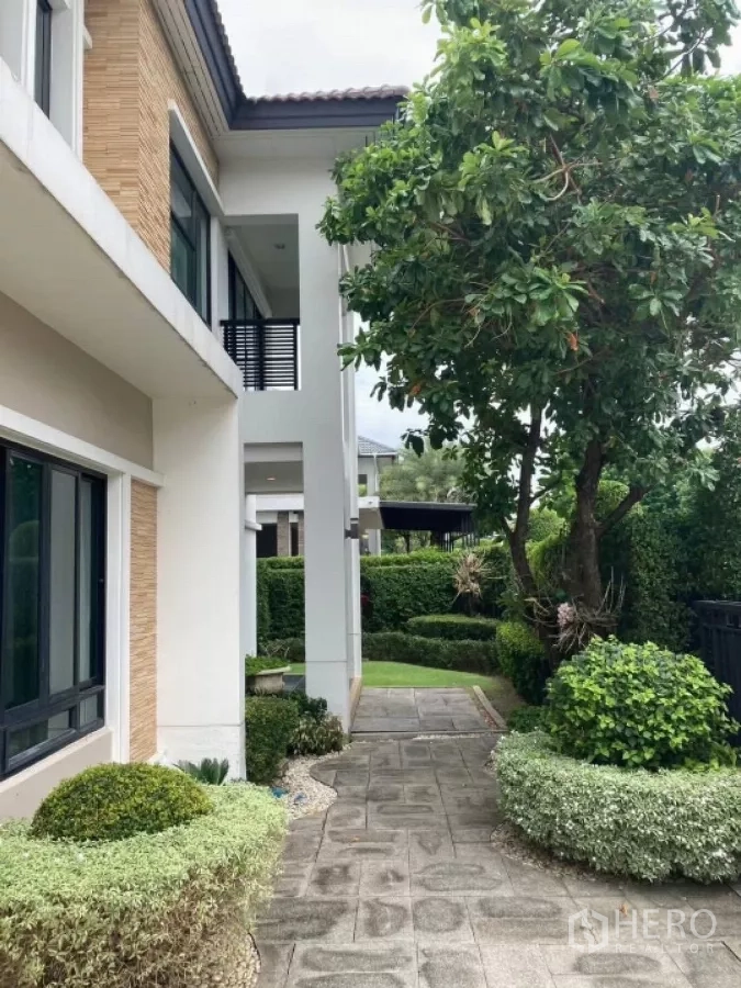 Detached House for rent in Mueang Nonthaburi, Nonthaburi - Shaded garden walkway along the side of the house with mature tree, hedges and paved path.