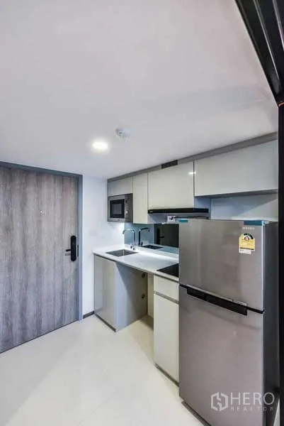 Condominium for rent in Huai Khwang, Bangkok - Compact entry kitchen with glossy cabinets, sink, microwave and stainless refrigerator.